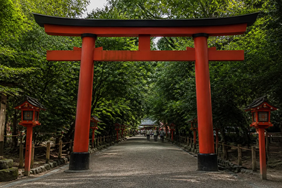 Entrée d’un sanctuaire shinto japonais avec torii rouge et allée bordée d’arbres