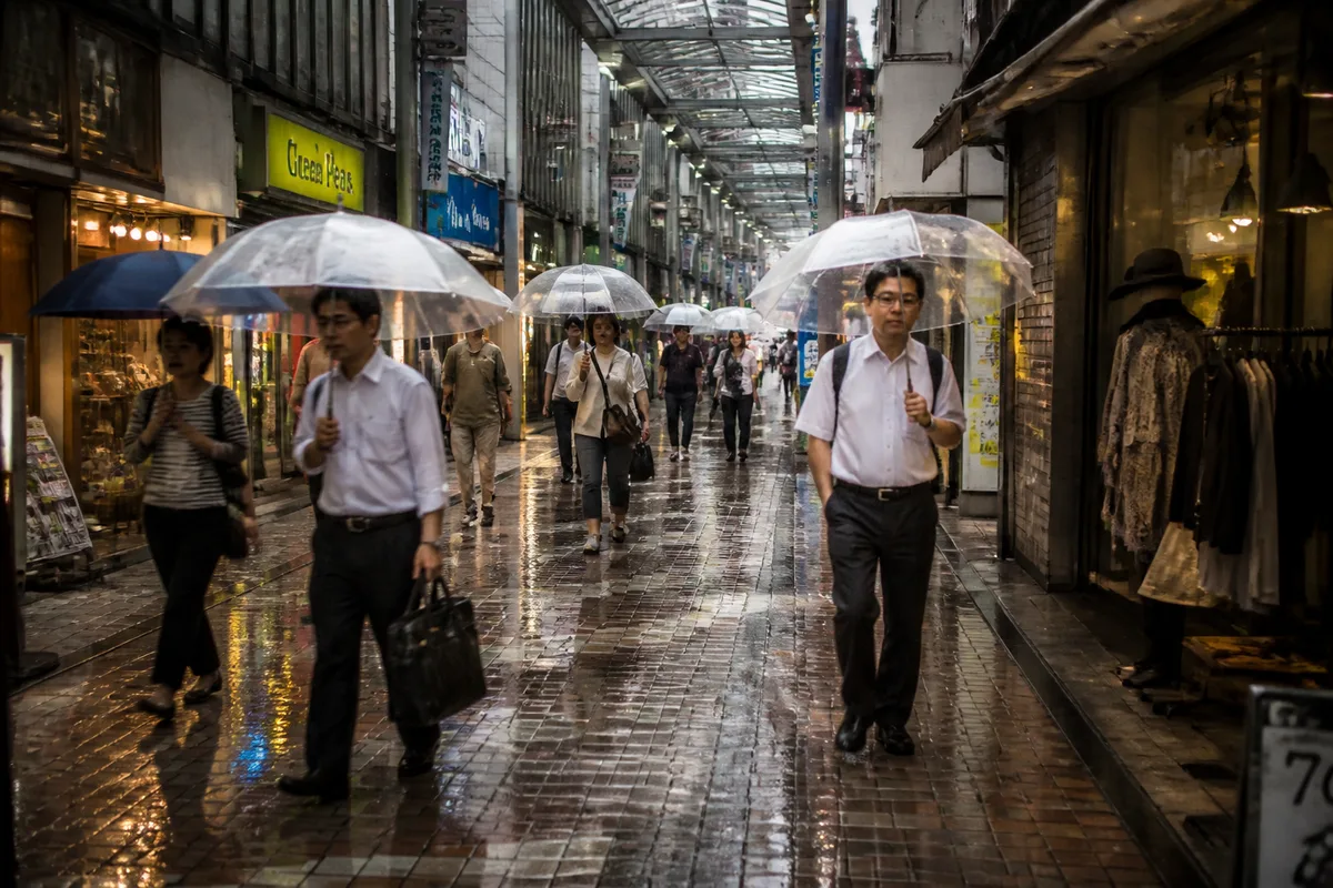 Visiteurs sous des parapluies dans une rue commerçante de Tokyo pendant une averse